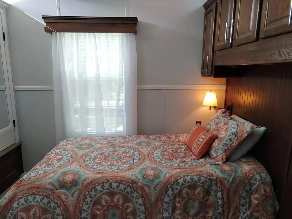 Bedroom with a queen-size bed, built-in cabinets, and natural light inside the Crimson Poppy tiny home.